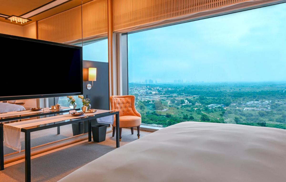 a bedroom with a large bed and a desk and a large window at Grand Hyatt Gurgaon in Gurgaon