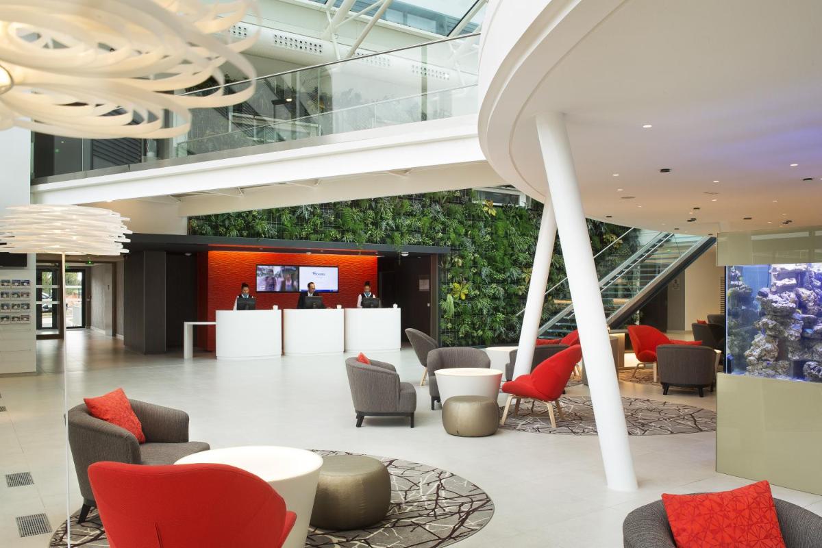 - un hall avec des chaises rouges et un mur vert dans l'établissement Oceania Paris Roissy CDG, au Mesnil-Amelot