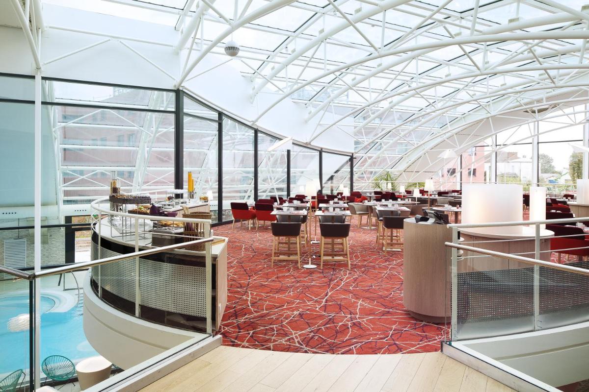 un restaurant avec un plafond en verre, des tables et des chaises dans l'établissement Oceania Paris Roissy CDG, au Mesnil-Amelot