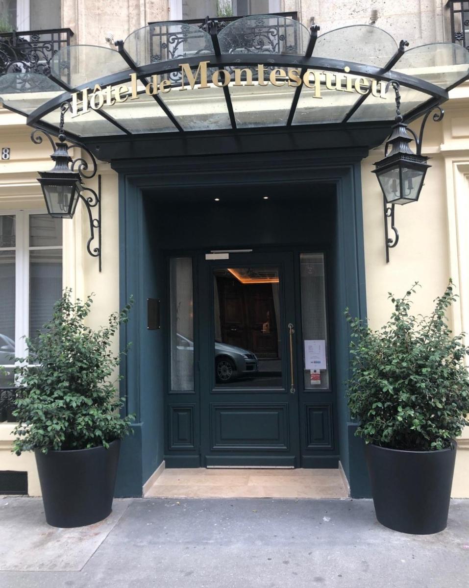 une porte d'entrée d'un immeuble avec deux plantes en pot dans l'établissement Hotel de Montesquieu, à Paris