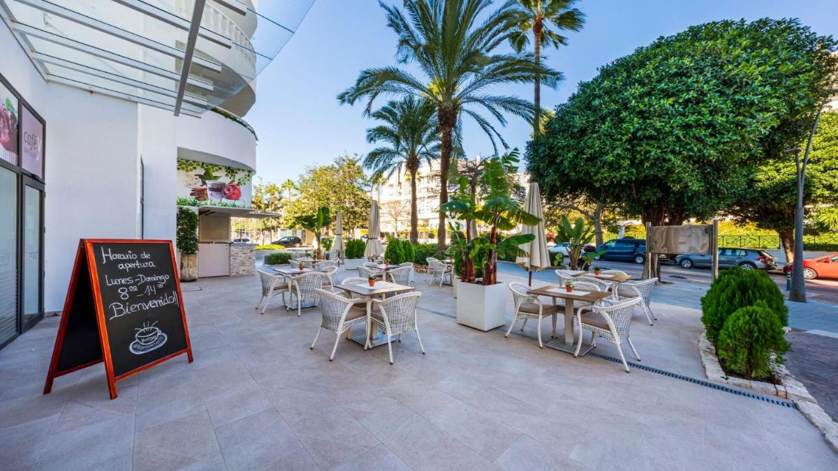Un restaurante con mesas y sillas y palmeras. en Hapimag Apartments Marbella, en Marbella