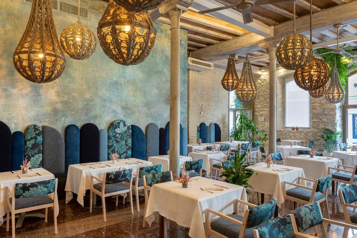Un restaurante con mesas y sillas blancas y candelabros. en Hotel Spa Porto Cristo, en Port de la Selva Un restaurante con mesas y sillas blancas y candelabros. en Hotel Spa Porto Cristo, en Port de la Selva