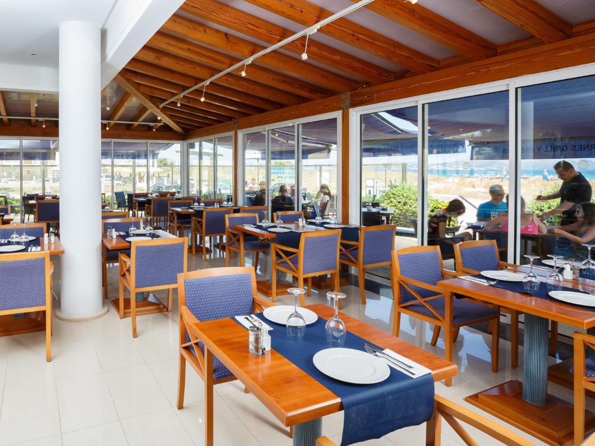 Un restaurante con mesas y sillas de madera y ventanas. en Aparthotel Dunes Platja, en Can Picafort