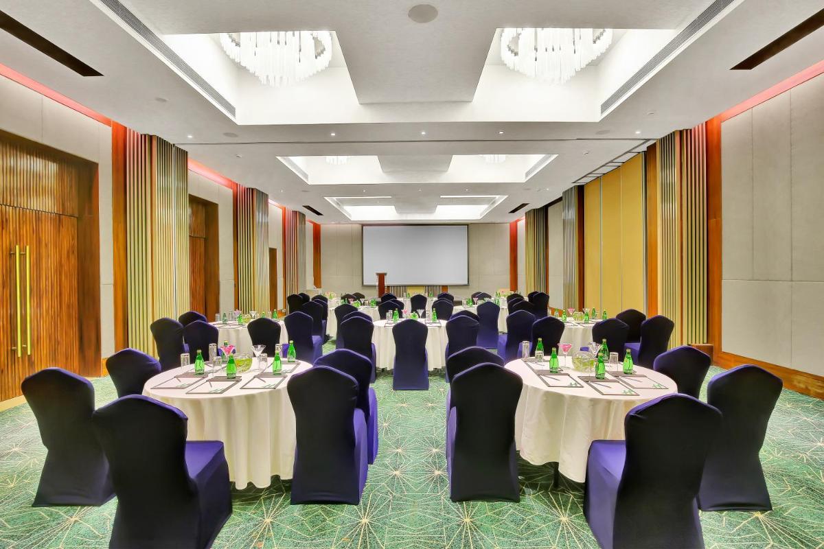 a conference room with tables and chairs and a screen at Holiday Inn Goa Candolim in Candolim a conference room with tables and chairs and a screen at Holiday Inn Goa Candolim in Candolim