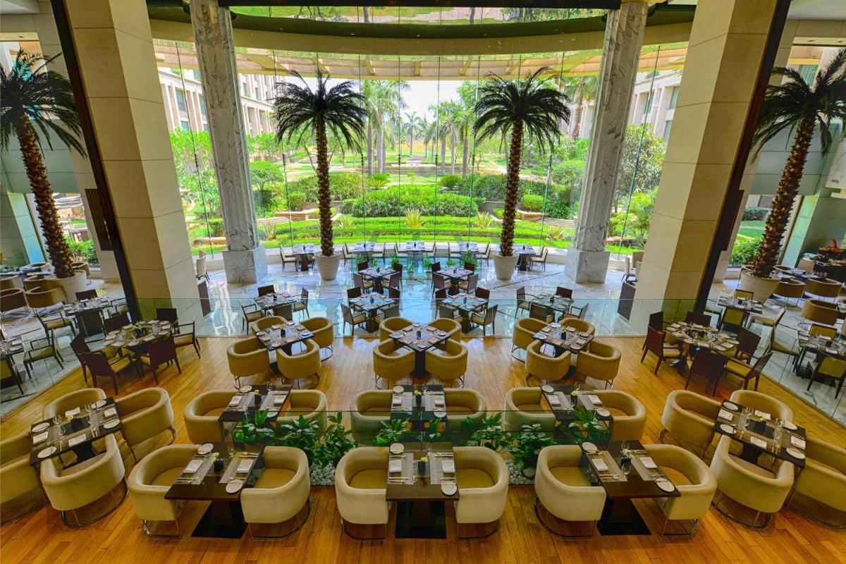 a restaurant with tables and chairs and palm trees at The Grand New Delhi in New Delhi a restaurant with tables and chairs and palm trees at The Grand New Delhi in New Delhi