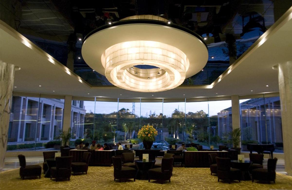 a large room with a large chandelier and tables and chairs at The Grand New Delhi in New Delhi a large room with a large chandelier and tables and chairs at The Grand New Delhi in New Delhi