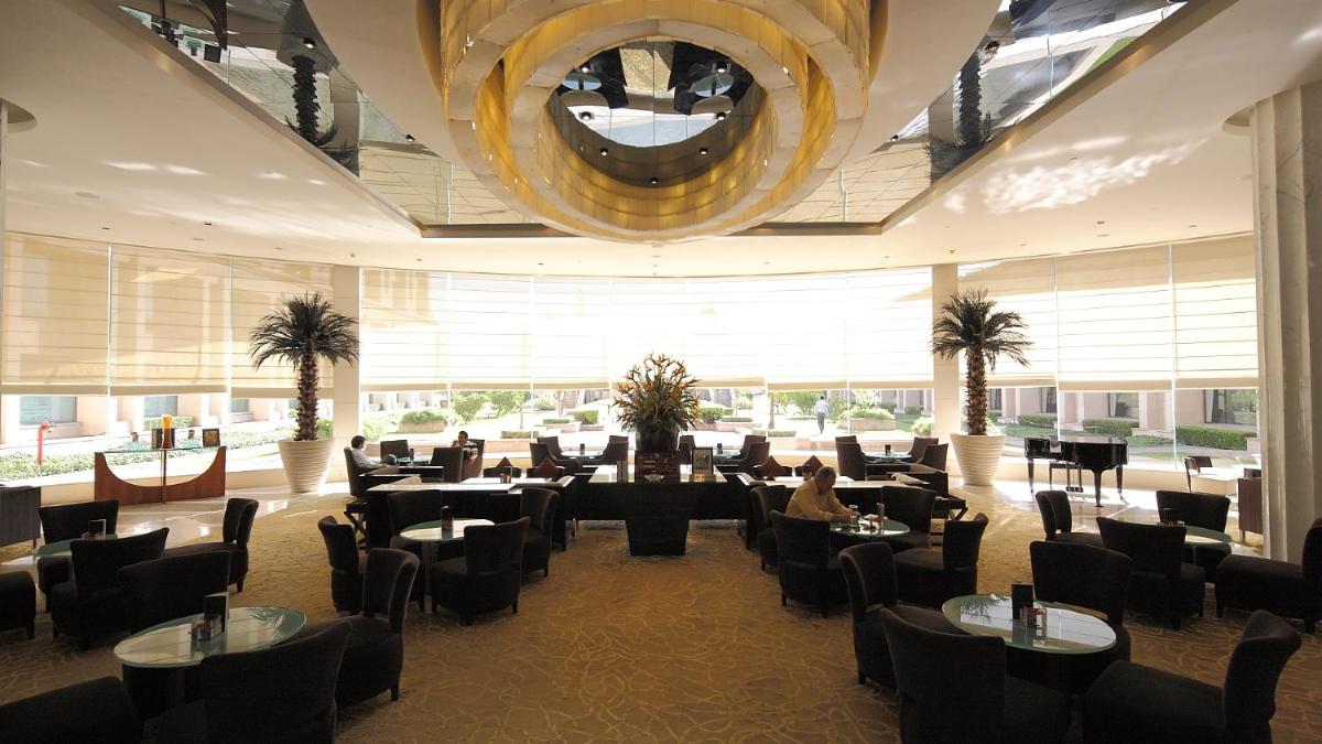 a restaurant with a large chandelier and tables and chairs at The Grand New Delhi in New Delhi a restaurant with a large chandelier and tables and chairs at The Grand New Delhi in New Delhi