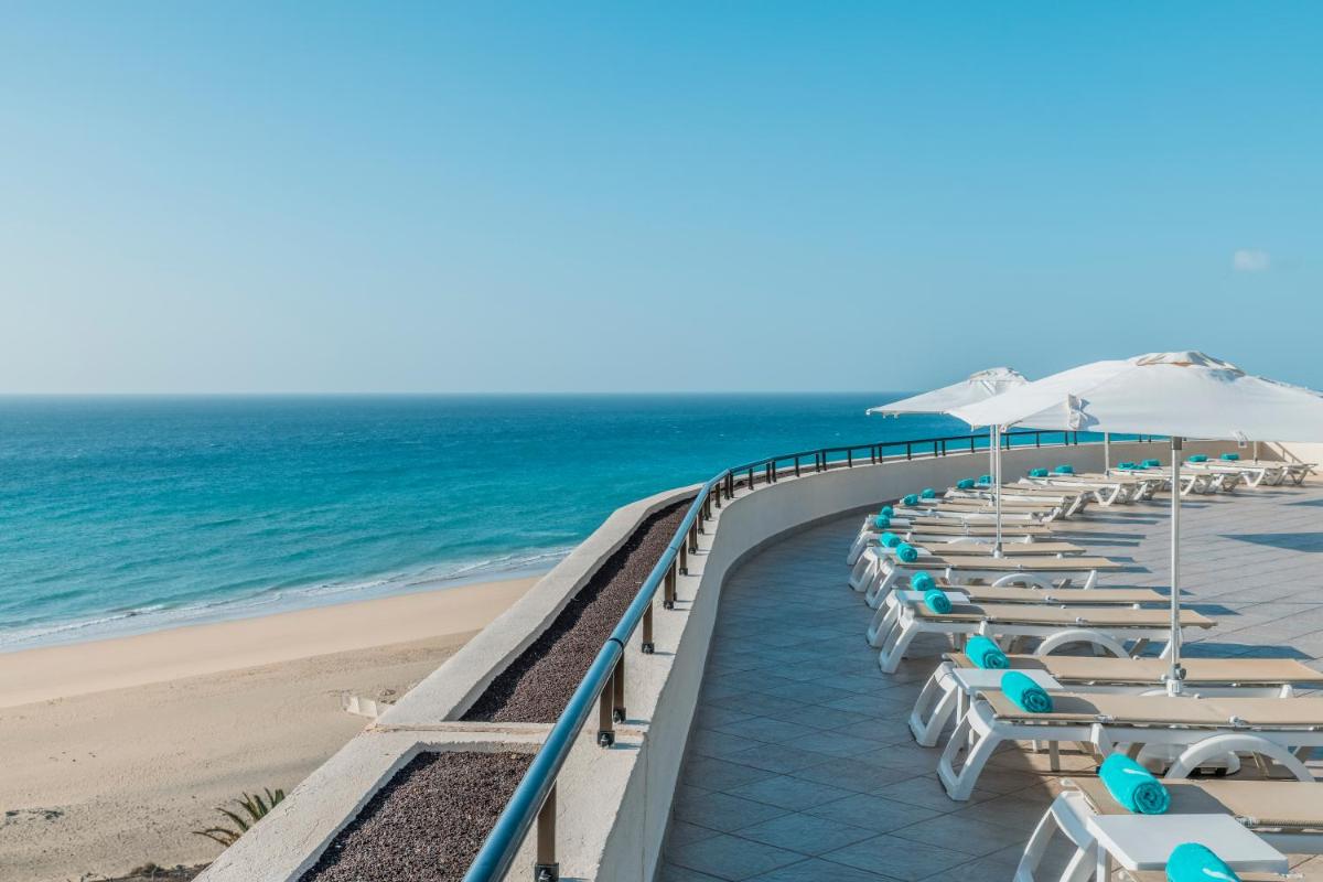 una fila de sillas y sombrillas en una playa en Iberostar Waves Playa Gaviotas All Inclusive, en Morro del Jable