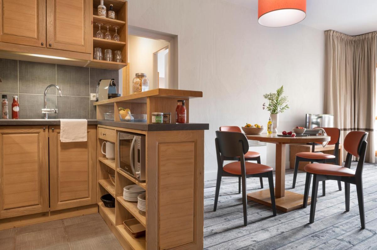 une cuisine avec des armoires en bois et une table avec des chaises dans l'établissement Résidence Pierre & Vacances Premium Les Terrasses d'Eos, à Flaine