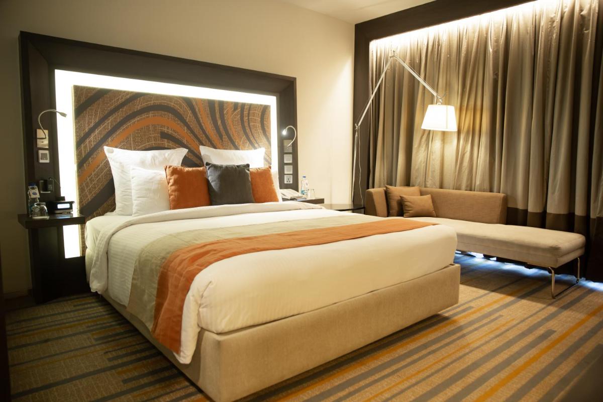 a hotel room with a large bed and a chair at Novotel Kolkata Hotel and Residences in Kolkata a hotel room with a large bed and a chair at Novotel Kolkata Hotel and Residences in Kolkata