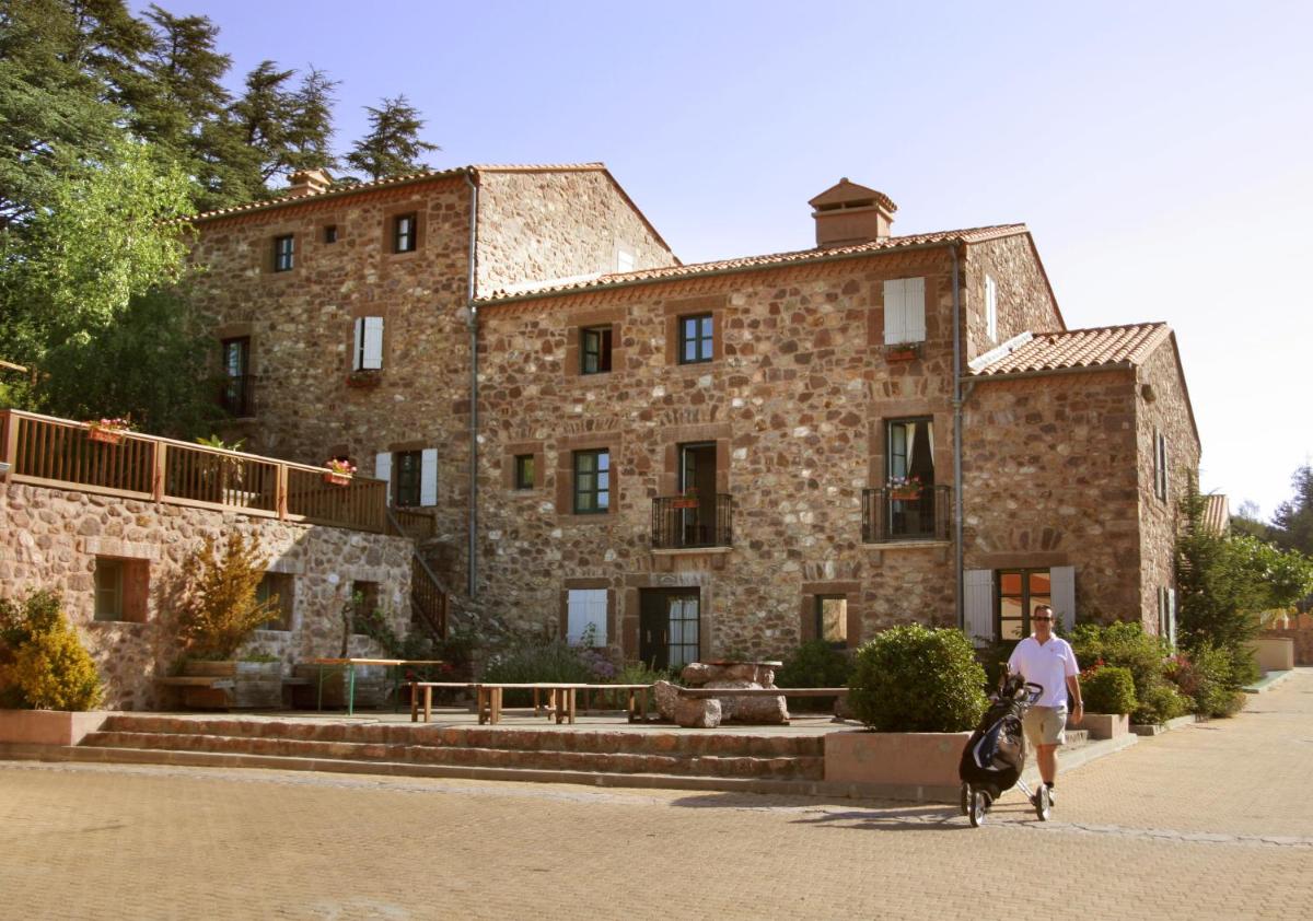 une femme promenant un chien devant un grand bâtiment en pierre dans l'établissement Le Domaine de Falgos Golf & Spa, à Saint-Laurent-de-Cerdans