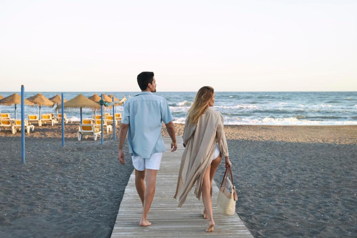 un hombre y una mujer caminando por una pasarela de madera en la playa en Iberostar Waves Málaga Playa, en Torrox Costa