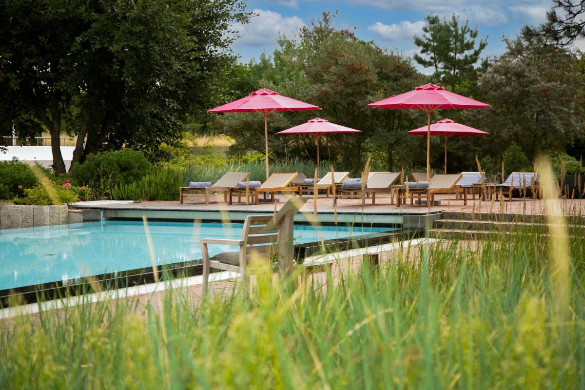 ein Swimmingpool mit Stühlen und Sonnenschirmen in der Unterkunft Aalernhüs hotel & spa in Sankt Peter-Ording