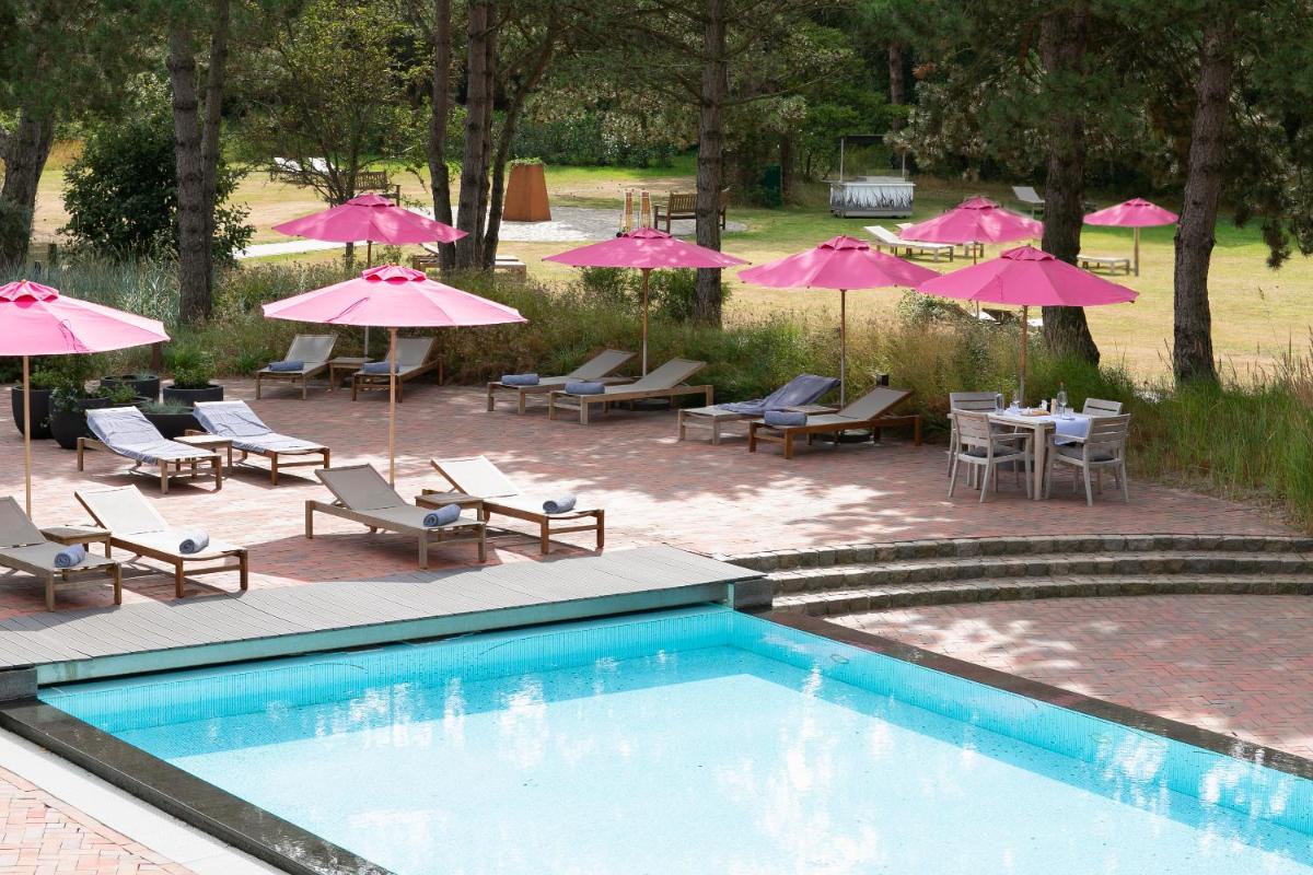 einen Pool mit Stühlen, Tischen und rosa Sonnenschirmen in der Unterkunft Aalernhüs hotel & spa in Sankt Peter-Ording