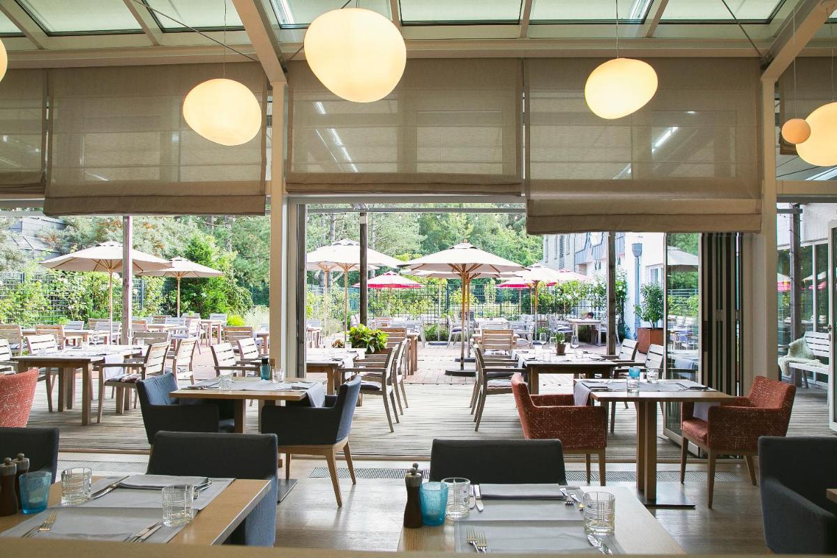 ein Restaurant mit Tischen, Stühlen und Sonnenschirmen in der Unterkunft Aalernhüs hotel & spa in Sankt Peter-Ording