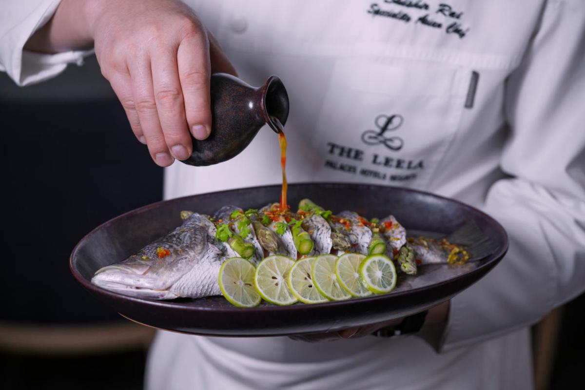 a person holding a plate with a fish and vegetables at The Leela Bhartiya City Bengaluru in Bengaluru a person holding a plate with a fish and vegetables at The Leela Bhartiya City Bengaluru in Bengaluru
