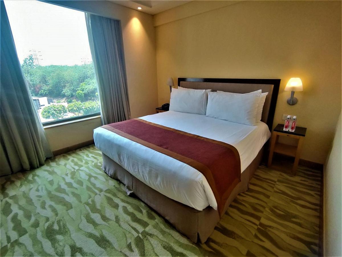 a hotel room with a large bed and a window at The Grand New Delhi in New Delhi a hotel room with a large bed and a window at The Grand New Delhi in New Delhi