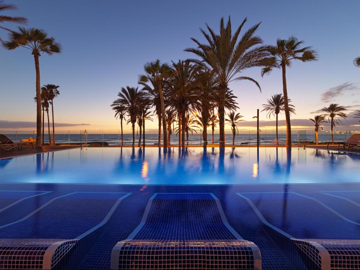 una piscina con palmeras y el océano en H10 Conquistador, en Playa de las Américas