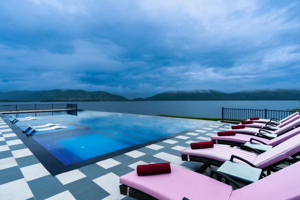 a pool with lounge chairs next to the water at ZANA Lakeview Resort - most scenic lakeside resort in Udaipur