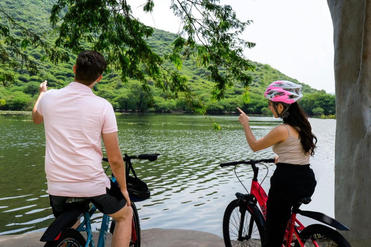 a man and a woman on bikes in front of a lake at ZANA Lakeview Resort - most scenic lakeside resort in Udaipur
