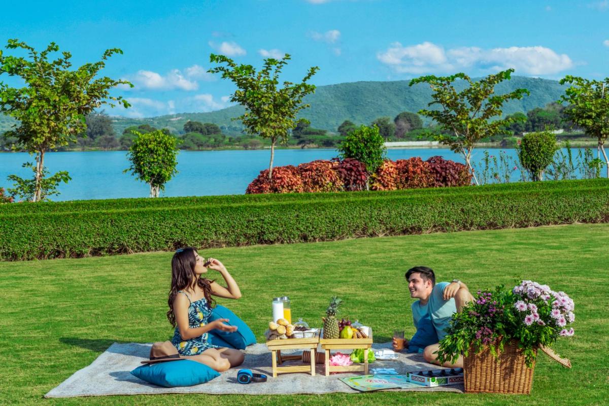 a man and woman sitting on a picnic blanket in the grass at ZANA Lakeview Resort - most scenic lakeside resort in Udaipur