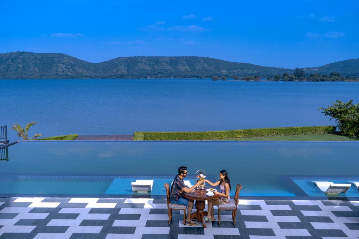 two people sitting at a table in front of a lake at ZANA Lakeview Resort - most scenic lakeside resort in Udaipur