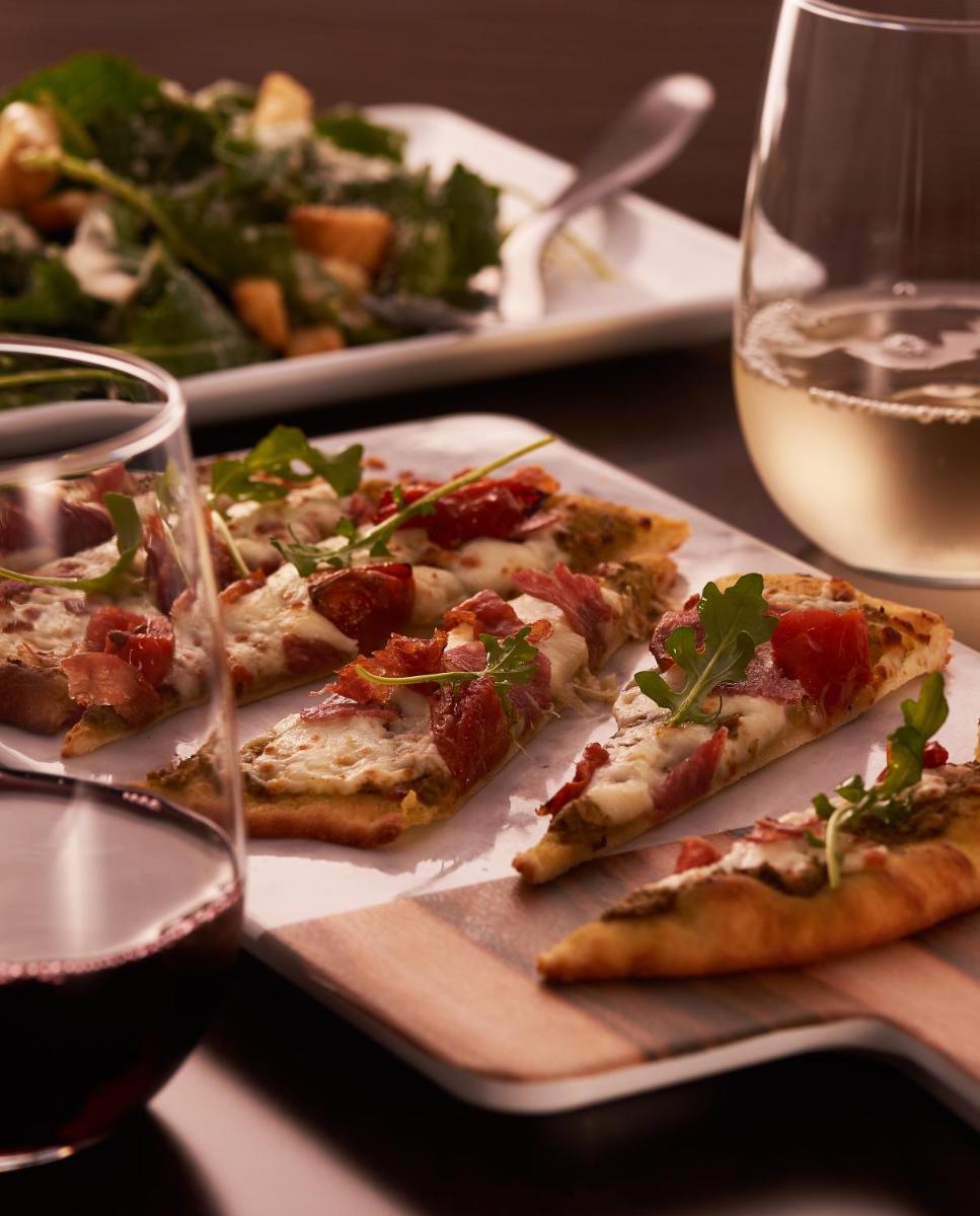 a table with three slices of pizza and a glass of wine at Hyatt Place Jaipur Malviya Nagar in Jaipur a table with three slices of pizza and a glass of wine at Hyatt Place Jaipur Malviya Nagar in Jaipur