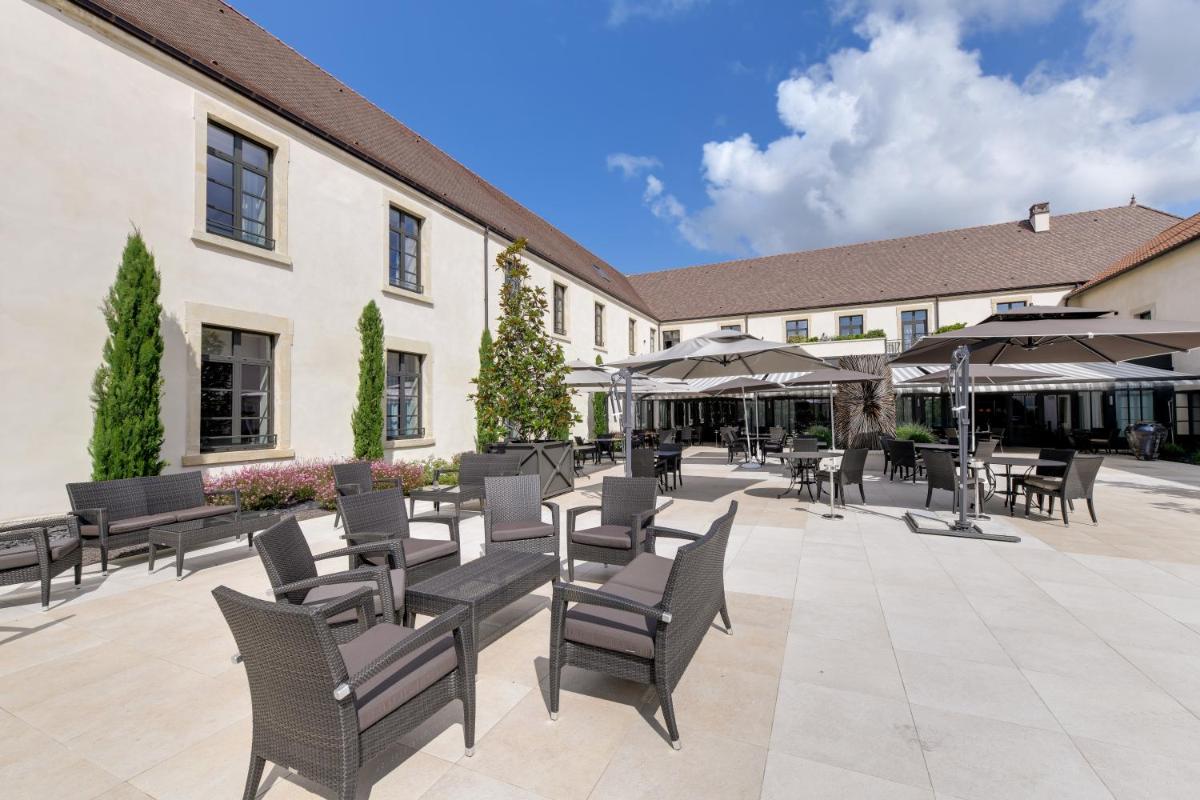 un patio avec des chaises, des tables et des parasols dans l'établissement Hôtel & Spa Les Sept Fontaines Best Western Premier, à Tournus