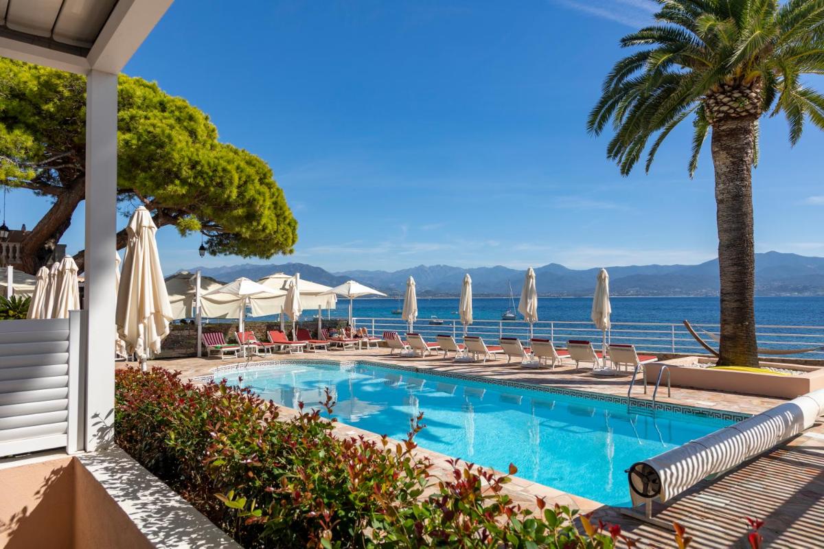 - une piscine avec chaises longues et parasols et l'océan dans l'établissement Hôtel Les Mouettes - Teritoria, à Ajaccio
