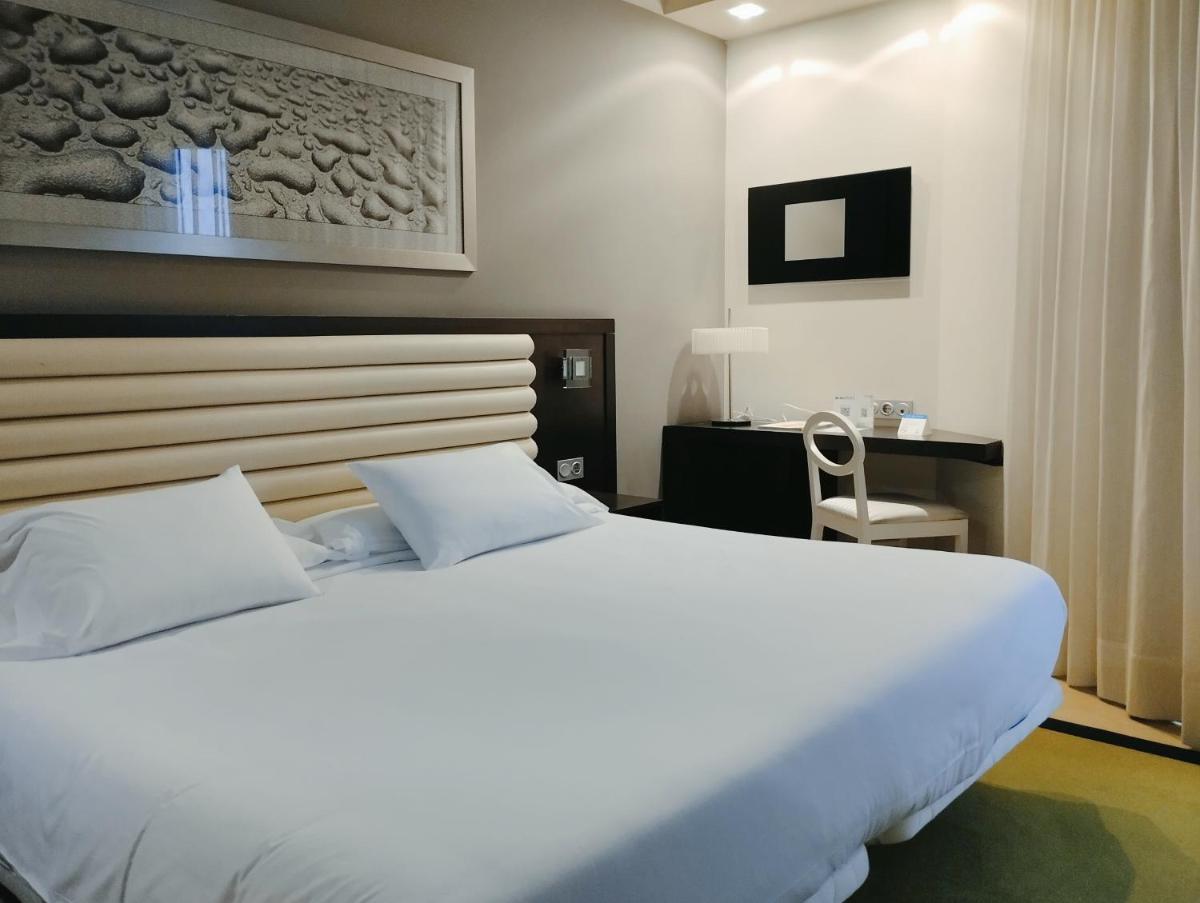 Un dormitorio con una gran cama blanca y un escritorio. en Hotel Bienestar Moaña, en Moaña