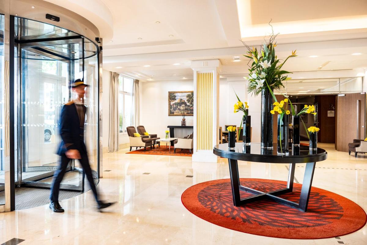 Un homme se promène dans un hall avec une table fleurie. dans l'établissement Relais Spa Val d'Europe, à Chessy 47 autres photos