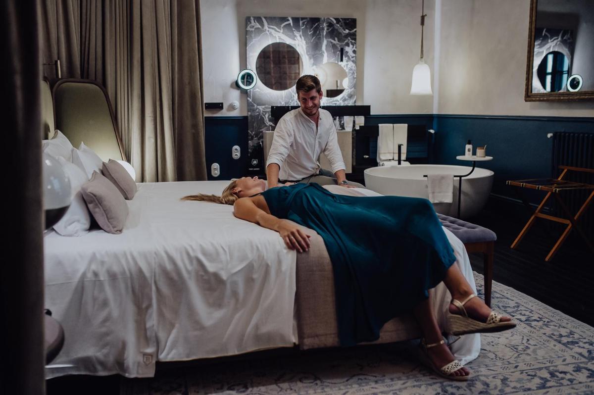 un hombre de pie junto a una mujer acostada en una cama en Can Bordoy Grand House Hotel GL Preferred Hotel, en Palma de Mallorca