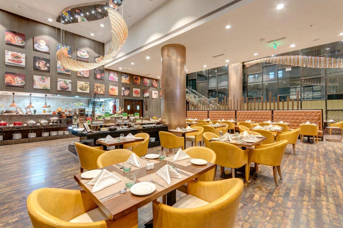 a restaurant with wooden tables and yellow chairs at Holiday Inn Kolkata Airport by IHG in Kolkata