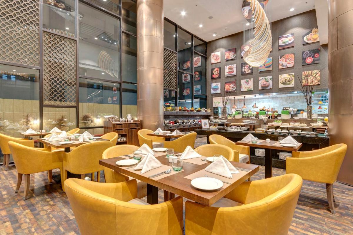 a restaurant with wooden tables and yellow chairs at Holiday Inn Kolkata Airport by IHG in Kolkata