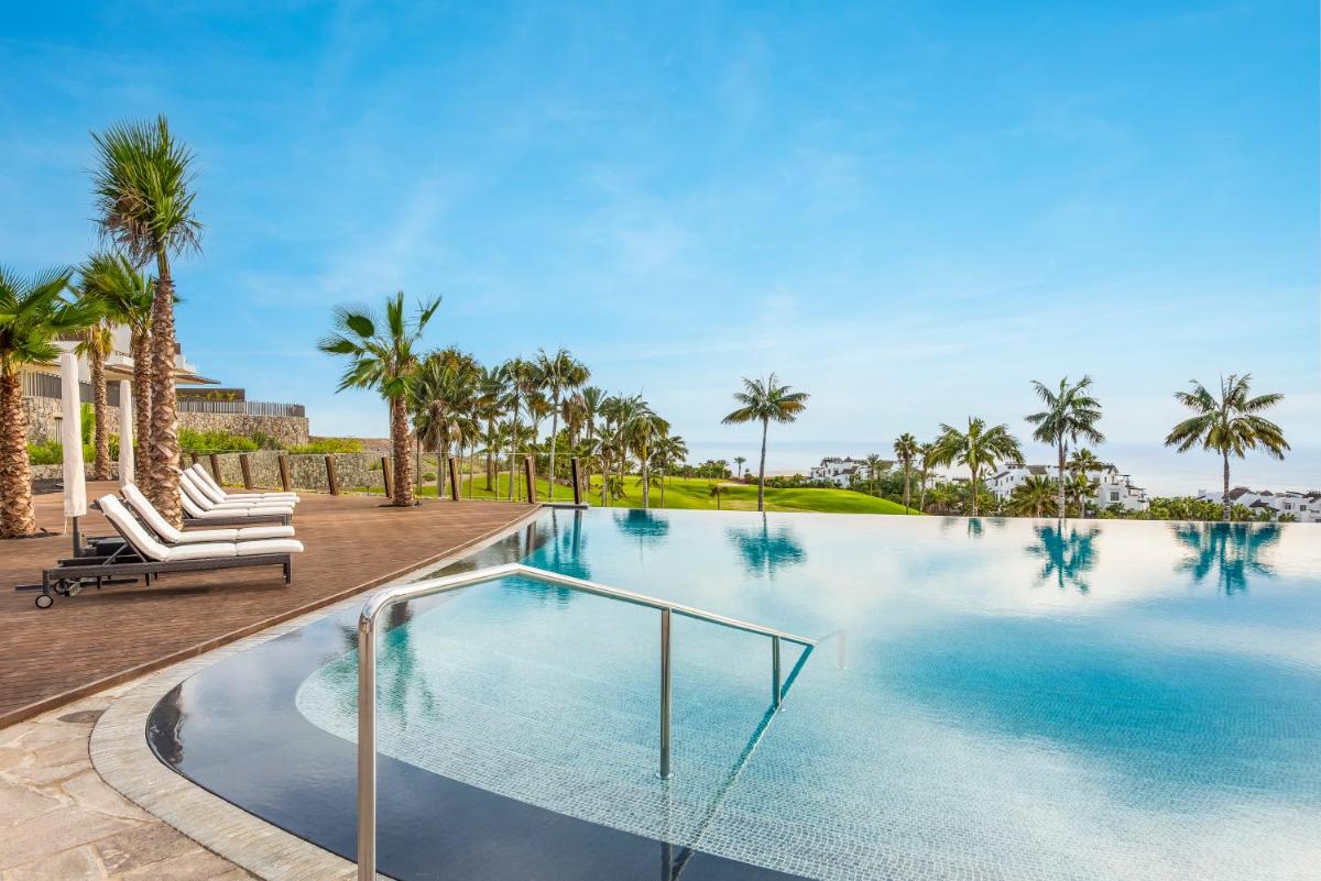 una piscina con palmeras al fondo en Los Jardines de Abama Suites & Villas, en Guía de Isora