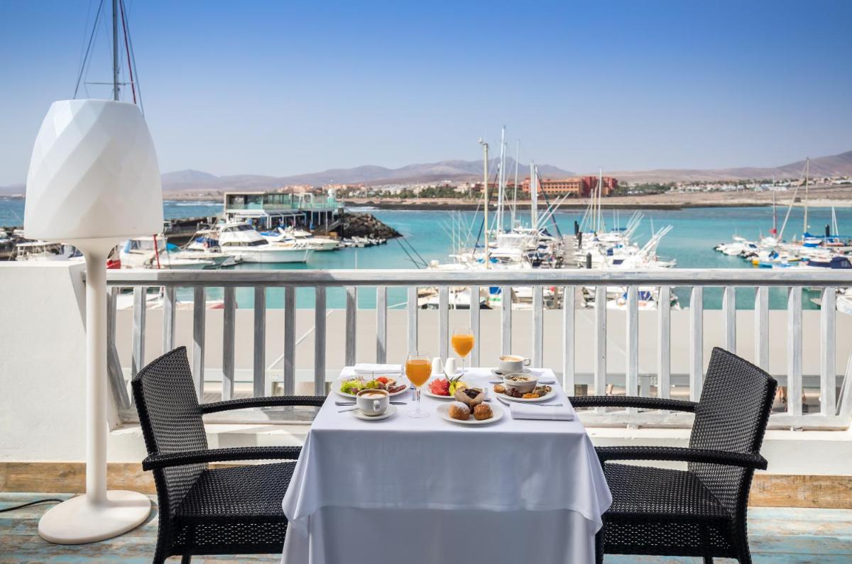 una mesa con comida y bebida en un balcón con puerto deportivo en Barceló Fuerteventura Royal Level, en Caleta de Fuste