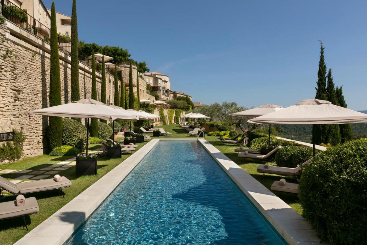 une piscine avec chaises et parasols à côté d'un bâtiment dans l'établissement Airelles Gordes, La Bastide, à Gordes