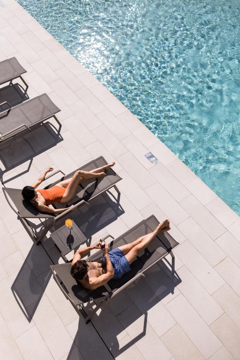 Dos personas tumbadas en las mesas junto a una piscina en Petit Sagitario Adults only, en Ciutadella