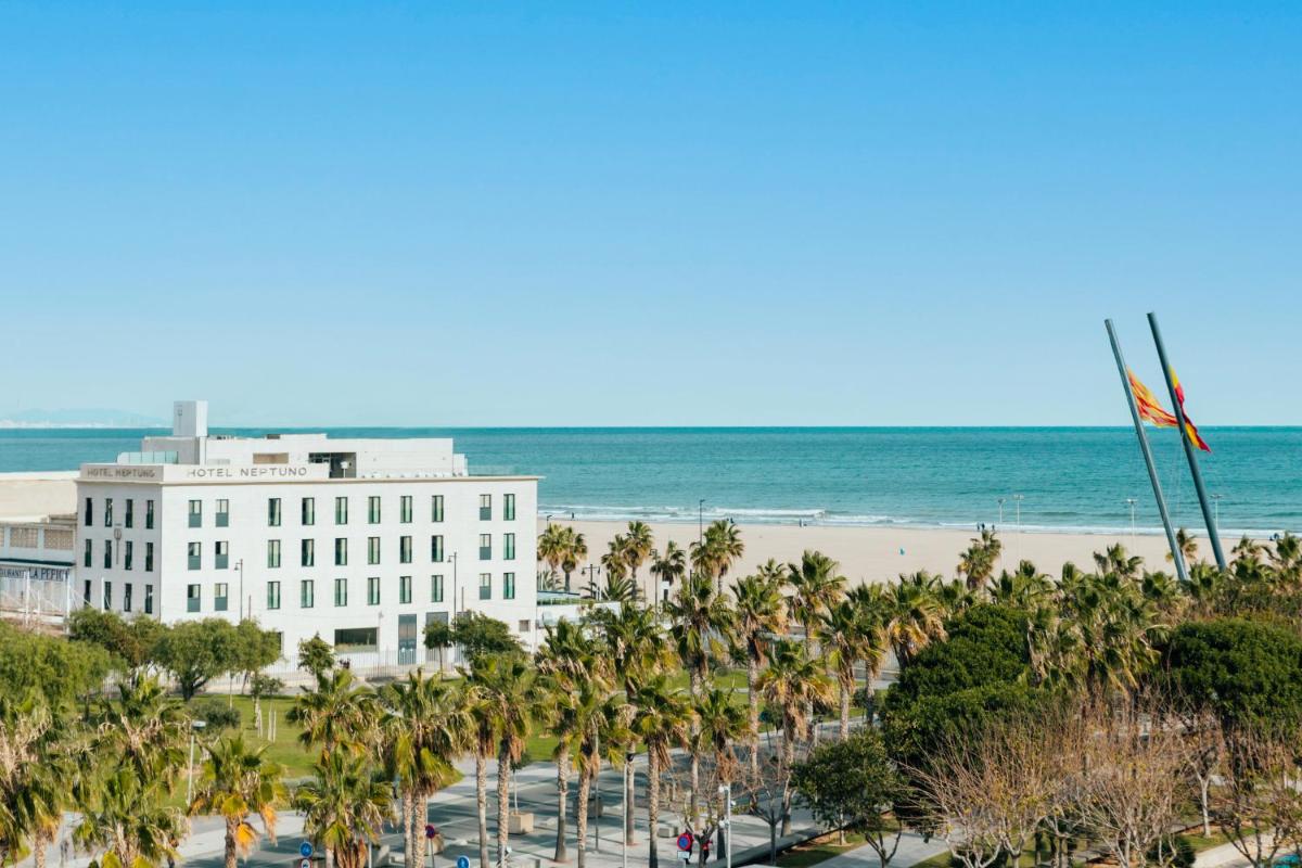 Un edificio en la playa con palmeras y el océano. en Hotel Neptuno Playa & Spa, en Valencia