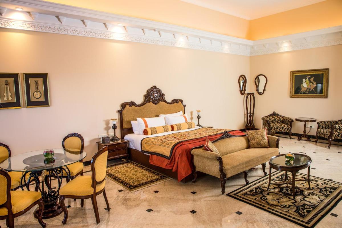 a bedroom with a bed and chairs and a table at The Lalit Laxmi Vilas Palace in Udaipur
