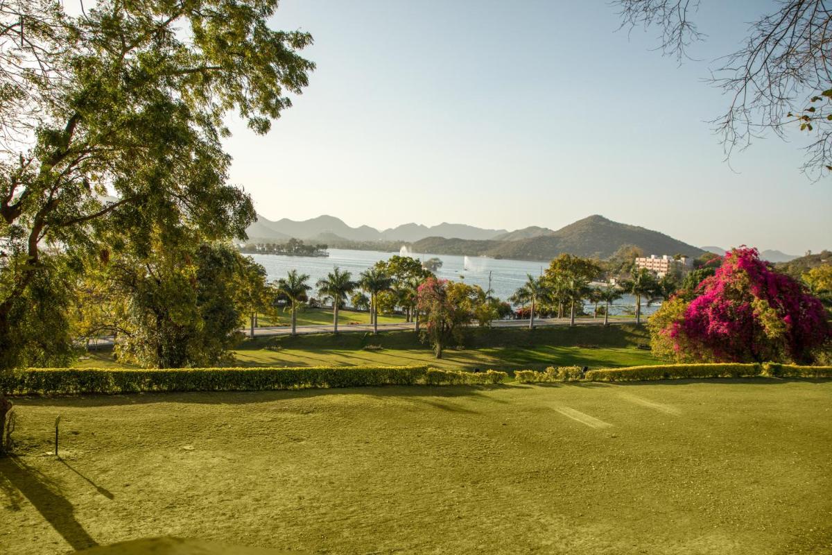 a park with a lake and mountains in the background at The Lalit Laxmi Vilas Palace in Udaipur