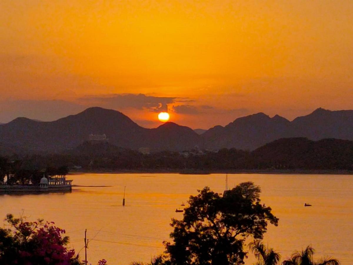 a sunset on the water with mountains in the background at The Lalit Laxmi Vilas Palace in Udaipur
