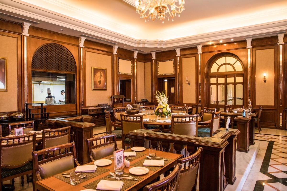 a restaurant with wooden tables and chairs and a chandelier at The Lalit Laxmi Vilas Palace in Udaipur