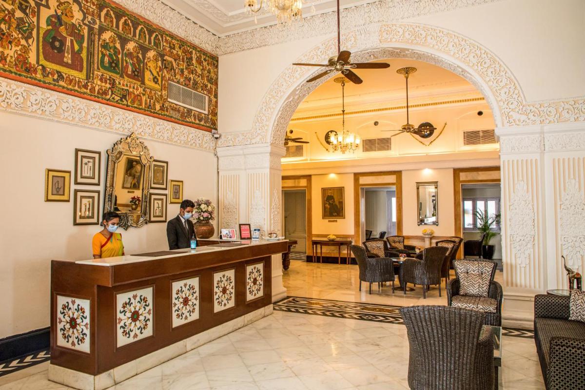 a man standing at a counter in a lobby with a dining room at The Lalit Laxmi Vilas Palace in Udaipur