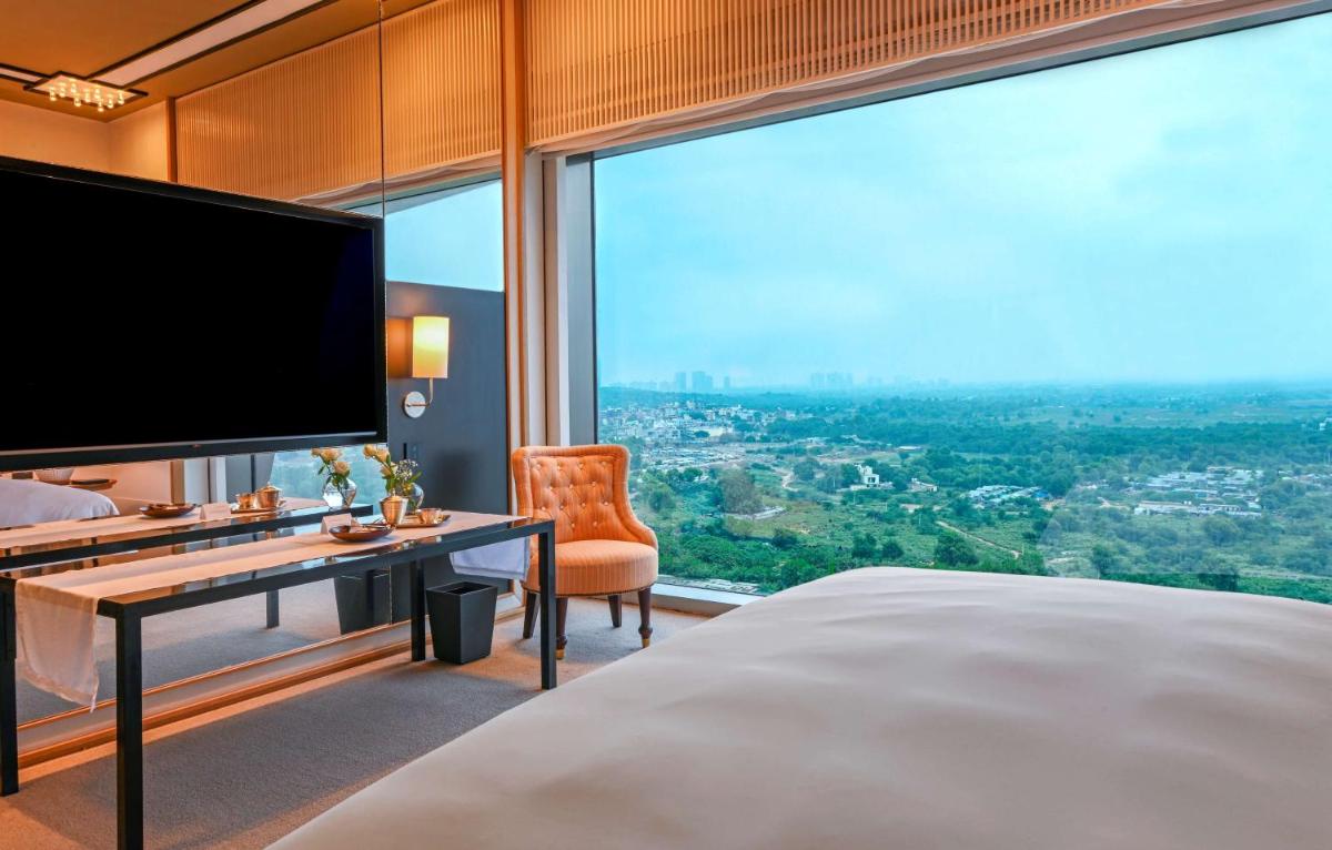 a bedroom with a large bed with a desk and a large window at Grand Hyatt Gurgaon in Gurgaon