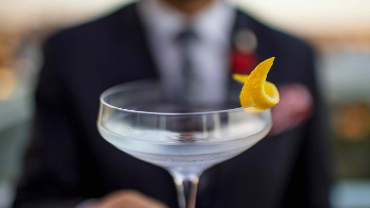 a man in a suit holding a glass with an orange peel on it at InterContinental Marine Drive Mumbai by IHG in Mumbai