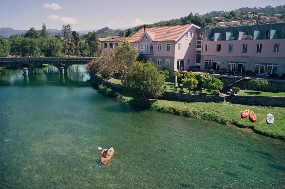 um rio com três canoas na água ao lado de prédios em Ribeira Collection Hotel by Piamonte Hotels em Arcos de Valdevez