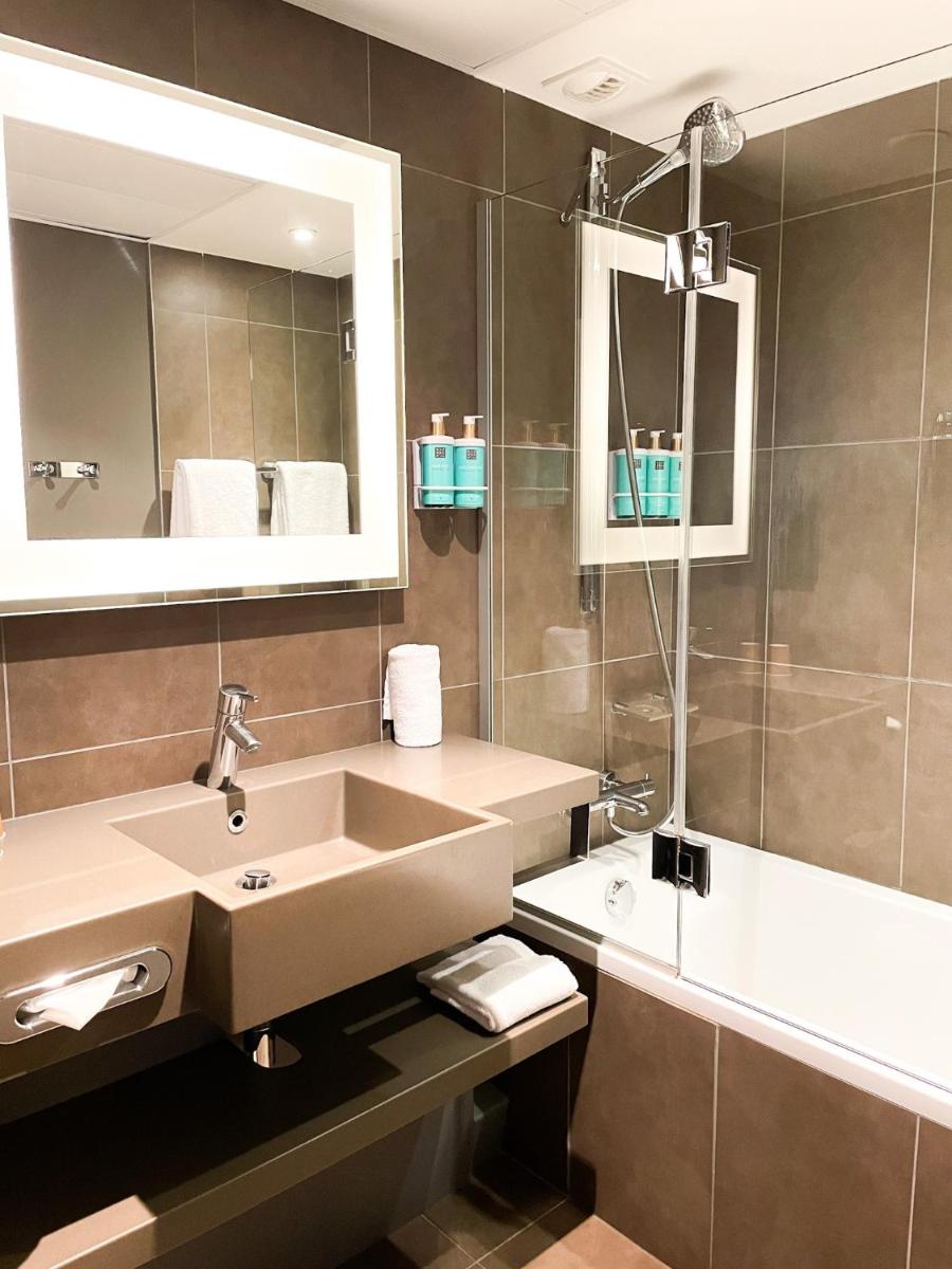 une salle de bains avec lavabo, miroir et baignoire dans l'établissement Novotel Fontainebleau Ury, à Ury
