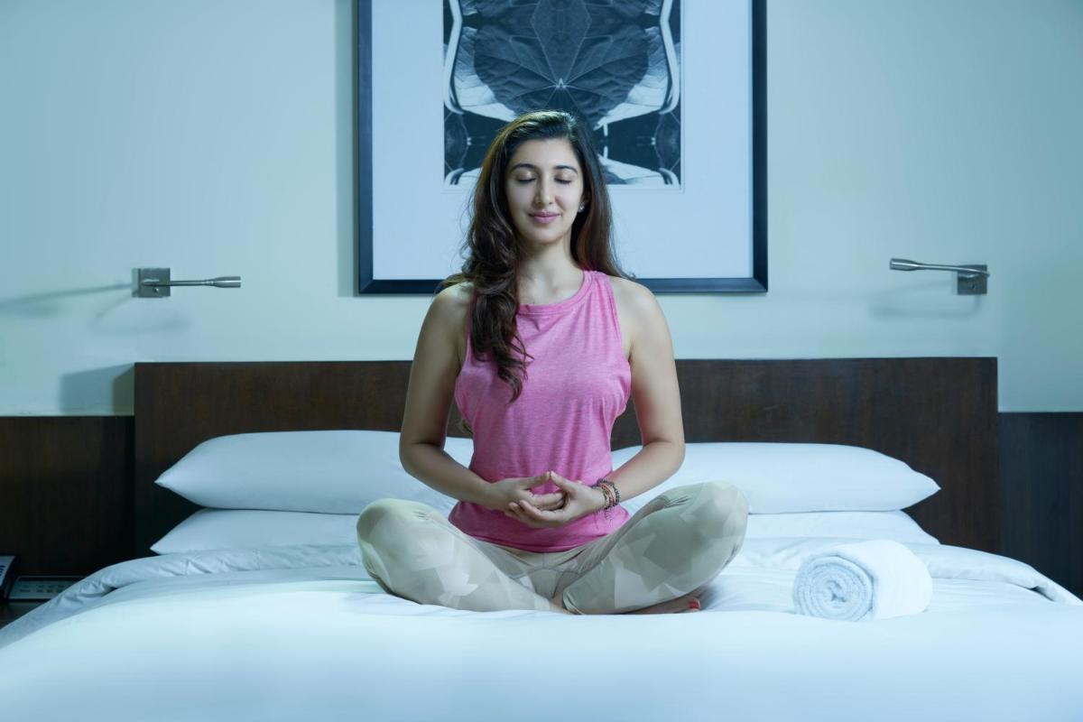 a woman sitting on a bed in meditation at Hyatt Hyderabad Gachibowli in Hyderabad