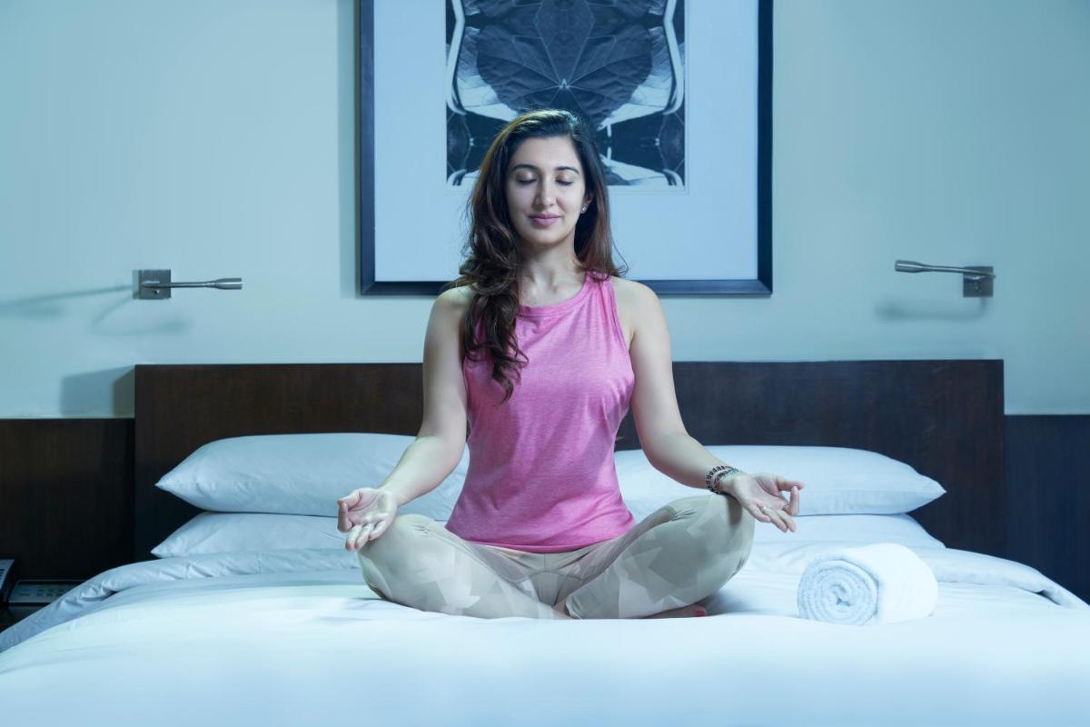 a woman sitting on a bed in meditation at Hyatt Hyderabad Gachibowli in Hyderabad